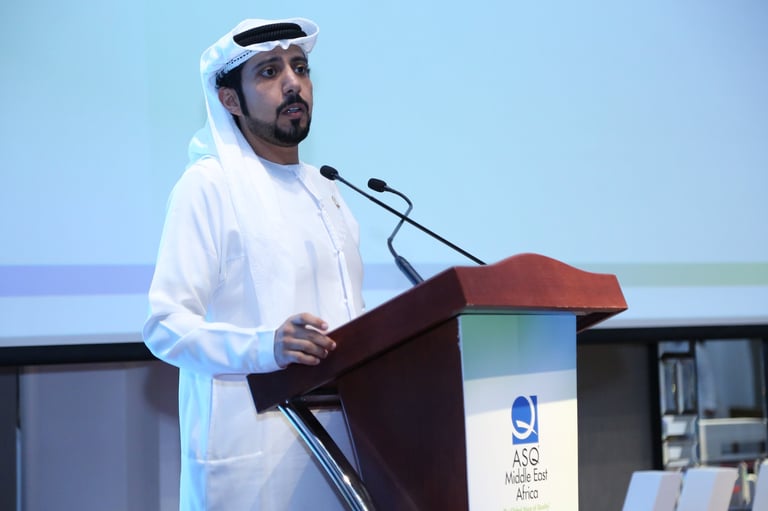 Man in traditional white Emirati dress speaking at a podium with microphone during a presentation